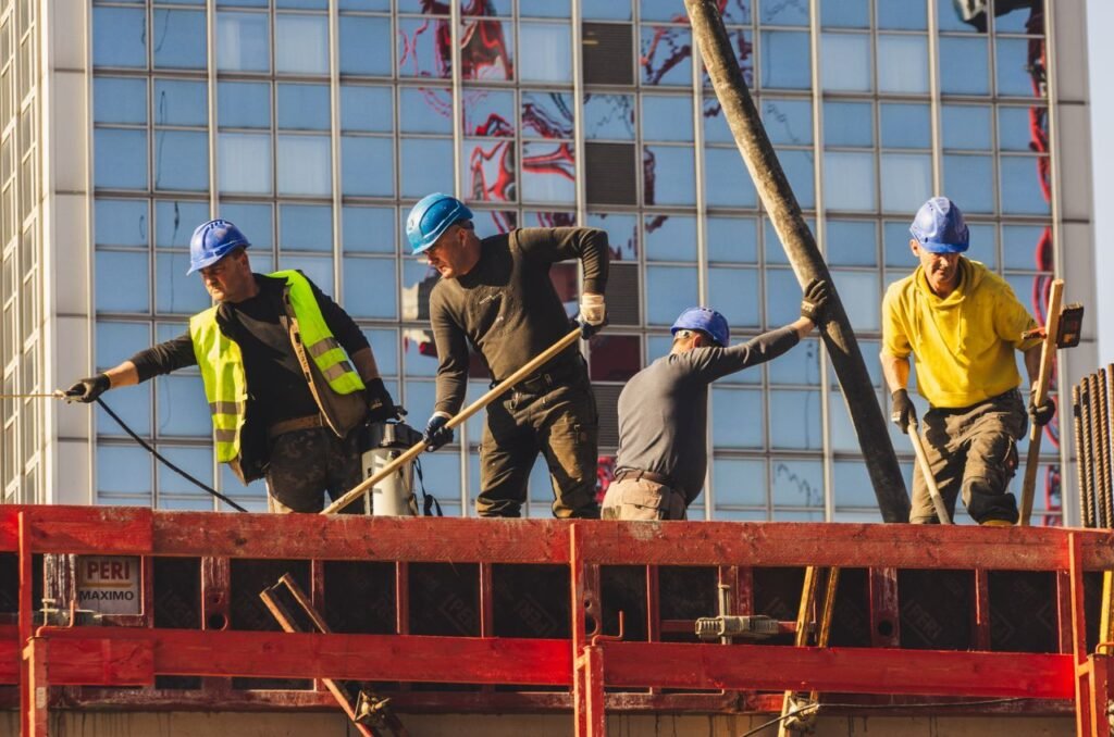 Impuestos en la Construcción A group of construction workers in safety gear actively working on a high-rise building site.